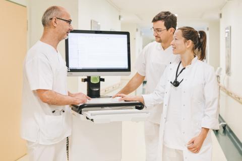 Visite auf der Station der Inneren Medizin, Medizin und Pflege im Gespräch am Visitenwagen.