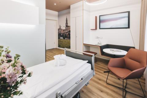 Wahlleistungszimmer im Krankenhaus St. Joseph-Stift Dresden: Eindruck mit Blick in den Raum aus Richtung Bett auf Sitzecke, Flachbildschirm-Fernseher und Flurbereich.