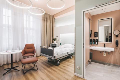 Wahlleistungszimmer im Krankenhaus St. Joseph-Stift Dresden: Blick in das Zimmer mit Bett und Sitzecke, rechts durch die offene Tür ein Blick in das angrenzende Badezimmer, links im Bild die Wandgestaltung mit Motiven der Dresdner Stadtansicht.