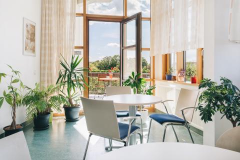 Blick in den großzügigen Wintergarten der Wochenstation mit Tischen, Stühlen, Balkon.