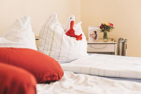 Detail Patientenzimmer auf der Wochenstation: Kopfkissen, rotes Stillkissen, Nachttisch im Fokus.