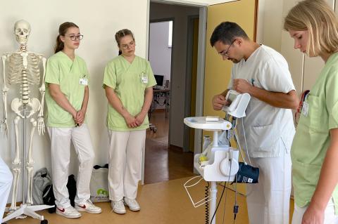 Praxisanleiter im Krankenhaus erklärt Freiwilligen die Vitalwerte auf dem Monitor.