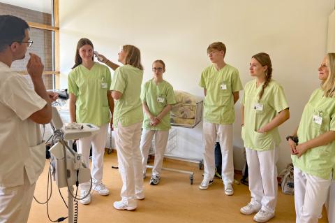 Einführungswoche für Freiwillige: Schulung durch Praxisanleiter mit Selbstversuch im Fiebermessen. Mehrere Freiwillige und Praxisanleiter in Dienstkleidung im Schulungsraum der medizinischen Berufsschule.