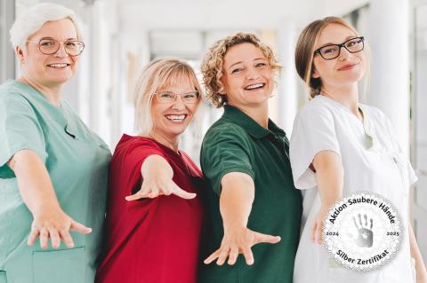 Siegel "Silbernes Zertifikat" der "Aktion Saubere Hände" erreicht. Das Siegel für 2024/2025 steht rechts auf einem Bild mit vier Pflegefachkräften aus unterschiedlichen Bereichen unseres Krankenhauses, die ihre sauberen Hände in die Kamera halten.