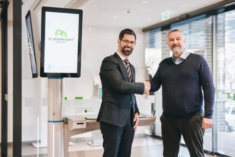 Roman Wygas, Vertriebsleiter bei der DeGIV GmbH und Jens Wohlrabe, Leiter Medizinische Dokumentation und Patientenverwaltung im St. Joseph-Stift, schütteln sich die Hände nach der erfolgreichen Installation des Gesundheitsterminals in der Zentralambulanz.