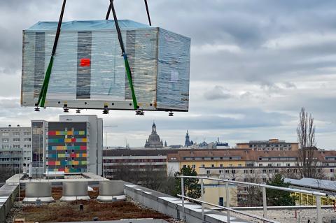 Projekt Nachhaltigkeit: Installation der Komponenten für die energetische Kühlung auf dem Krankenhausdach: Ein Kran befördert den Glaskasten dahin.