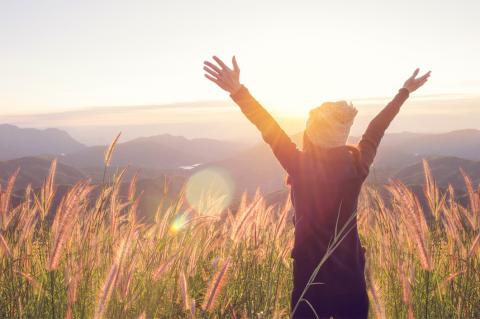 Endlich frei: Frau im Sonnenlicht, die Arme über den Kopf gestreckt. Symbolbild für Kopf frei – von mentaler Belastung.
