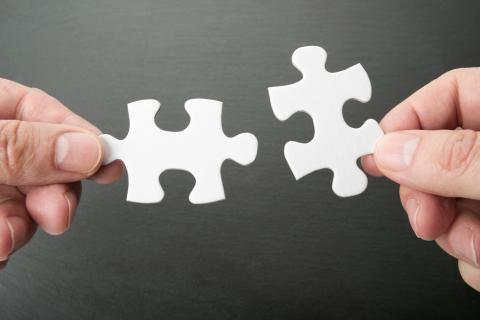 Hand in Hand – Hautpflege und Händehygiene. Kampagnenmotiv der diesjährigen Aktion zum gemeinsamen Tag der Händehygiene und Mitarbeitergesundheit: Zwei Hände führen zwei Puzzleteile zueinander, die sich ergänzen und kurz vor dem Ineinandergreifen sind.