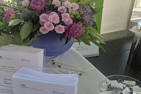 Eindruck vom Stand der Akademie im Foyer des Hygiene-Museums Dresden: Flyer, Kursprogramm und frische bunte Blumen vor dem grünen Rollup der Akademie für Palliativmedizin und Hospizarbeit.
