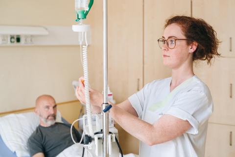 Schmerztherapie im St. Joseph-Stift – Schwester bei der Einstellung der Schmerzmedikation im Vordergrund, Patient im Hintergrund.