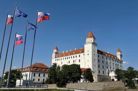 Burg Bratislava im Hintergrund, links vorn die slowakische Nationalflagge und EU-Flagge, strahlend blauer Sommerhimmel.