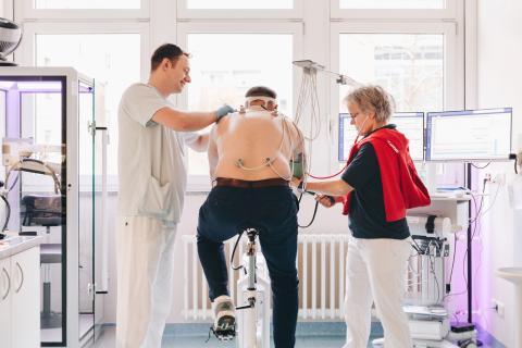 Sportmedizin am MVZ Forum Gesundheit Dresden, St. Joseph-Stift. Untersuchung während sportlicher Belastung, Blick in Untersuchungsraum mit Patient, Pfleger und Ärztin.