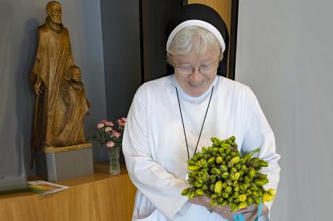 Ostern 2026: Schwester Antonia mit einem Arm voller gelber Tulpen als Gruß für die Kolleginnen und Kollegen am Ostersonntag, vor dem Seelsorgezimmer bzw. der Krankenhauskapelle; im Hintergrund die Figuren vom heiligen Joseph und dem Jesuskind als Statue.