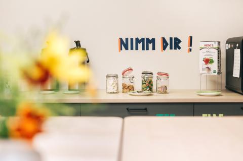 Akademie für Palliativmedizin und Hospizarbeit, Detail in der Gemeinschaftsküche mit offenem Sitz-, Arbeits- und Gesprächsbereich, Küchenwand mit Deko und Snacks.