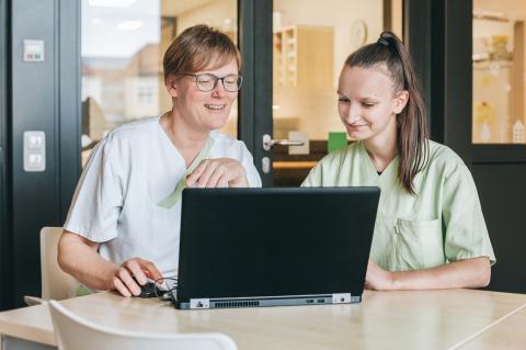 Medizinische Berufsfachschule am St. Joseph-Stift, Lernsituation im Pflegestützpunkt einer Station; Lehrerin und Auszubildende hinter dem Laptop bei der Dokumentation
