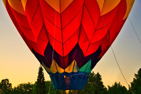 Patiententag Brustzentrum – Impression: Heißluftballon in rötlichen Farben, voller Helium, kurz vor dem Aufsteigen in den Sonnenuntergang, im Hintergrund Baumkronen.