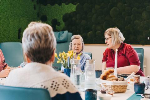 Tag der offenen Tür im Hospiz: Frühstückstisch im Tageshospiz, eine Pflegerin im Hospiz im Gespräch mit einem weiblichen Hospizgast am gedeckten Frühstückstisch.